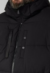 Schwarze Pufferjacke mit hohem Kragen, Reißverschluss und Druckknopf-Details. Verfügt über ein gestepptes Design und eine matte Oberfläche.