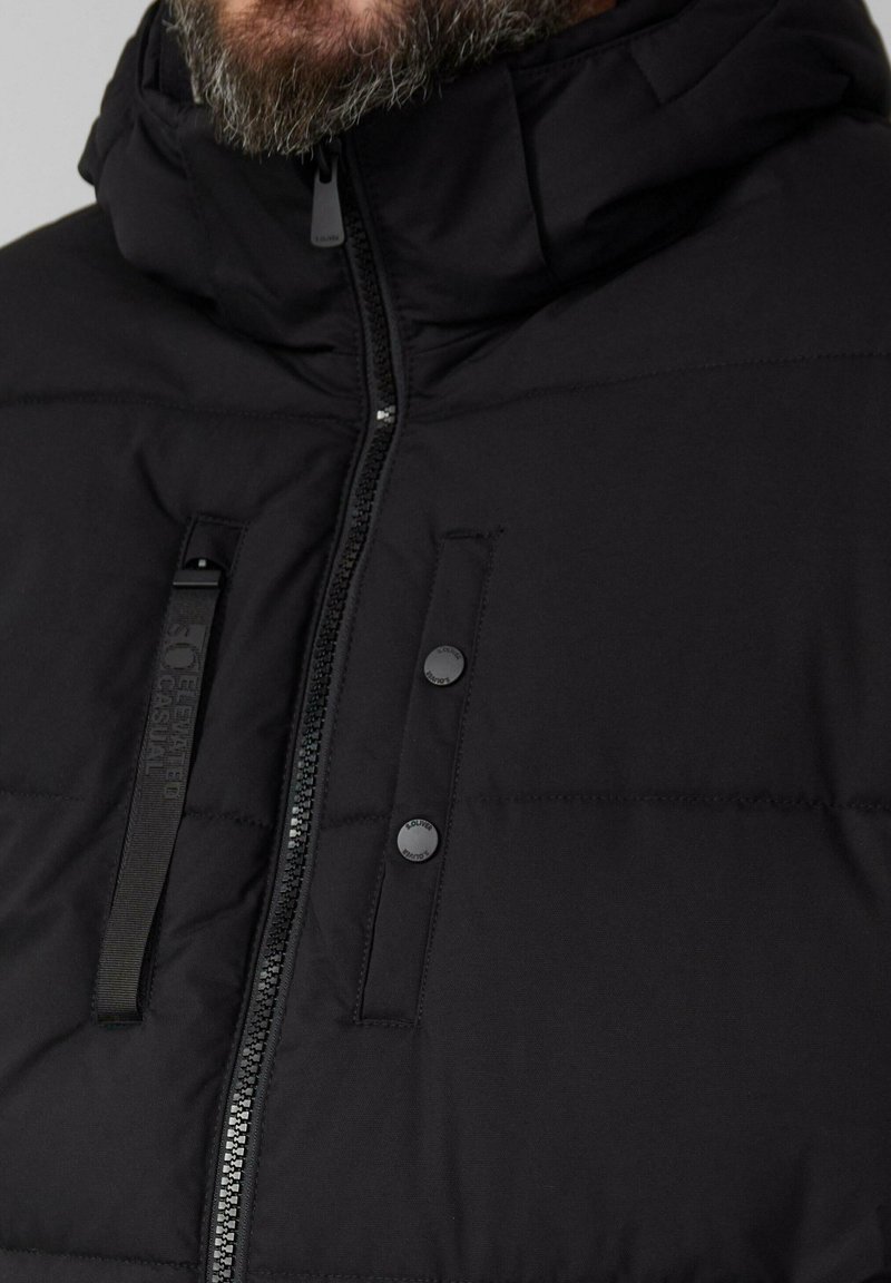 Schwarze Pufferjacke mit hohem Kragen, Reißverschluss und Druckknopf-Details. Verfügt über ein gestepptes Design und eine matte Oberfläche.