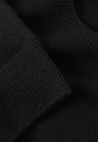 Gros plan d'un tissu tricoté noir avec un bord de manche côtelé et une texture douce.