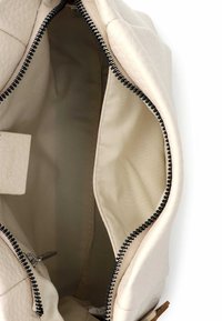 Beżowa torebka o fakturowanej powierzchni. Wnętrze wyłożone miękką tkaniną, z zamkiem błyskawicznym i małą kieszonką. Czarny detal zamka.