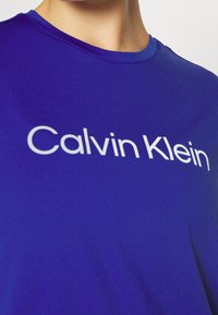 Camiseta de manga corta azul hecha de tela suave con el logo "Calvin Klein" en blanco a lo largo del pecho y un escote redondo.