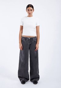 Biały prążkowany top z krótkim rękawem w połączeniu z luźnymi, wysokim stanem, ciemnoszarymi dżinsami. Gładka faktura, szerokie nogawki. Czarnie obuwie.