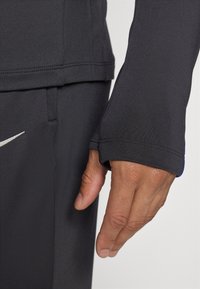 Schwarzes, sportliches Langarmshirt mit einer engen, glatten Textur. Verfügt über ein dezentes Logo und einen kontrastierenden blauen Akzent am Bündchen.
