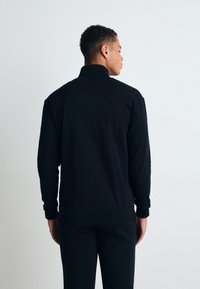 Svart langermet genser med høy krage, laget av glatt stoff. Har minimalistisk design og tettsittende mansjetter.