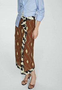Bruine gemusterde rok met abstracte crèmekleurige en zwarte ontwerpen, met een wikkelstijl en een lichte split. Gecombineerd met een lichtblauw shirt.