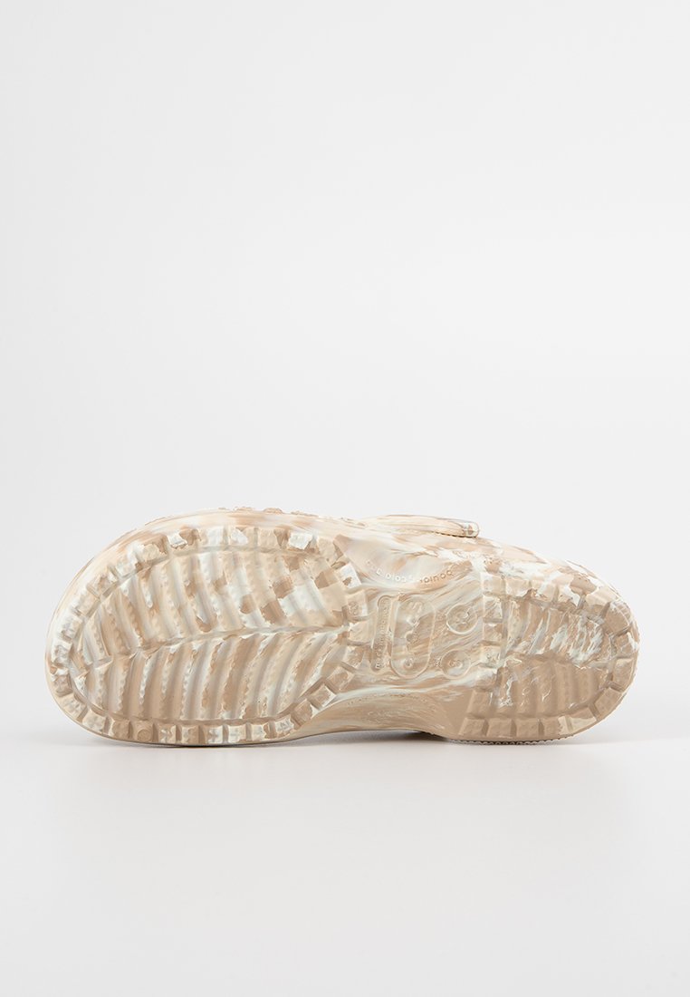 Suela de zapato en beige claro con patrón de agarre texturizado y detalle del logo. El material parece gomoso con un diseño de banda de rodadura visible para tracción.