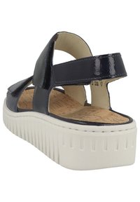 Laivaston sininen kiiltonahkasaapas, jossa on korkkinen pohjallinen, säädettävät hihnat ja paksu valkoinen kuminen alustallas, jossa on pystyrakenteet.