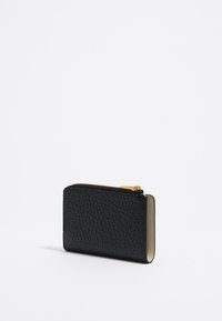 Portafoglio in pelle nera con superficie texturizzata, chiusura con zip e hardware in tonalità oro, caratterizzato da una forma rettangolare compatta.