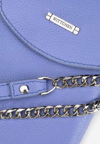 Blaue Lederhandtasche mit strukturierter Oberfläche, ausgestattet mit einem silbernen Logo aus Metall, Kettenriemen und abgesteppten Details entlang der Kanten.