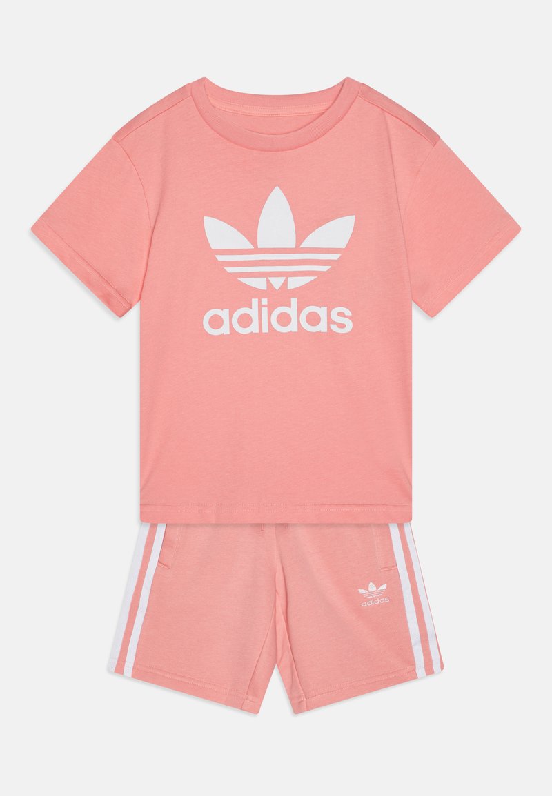 Rózsaszín Adidas póló fehér logóval, hozzá illő, fehér oldalsávokkal és logóval díszített sorttal párosítva. Puha anyagból készült.