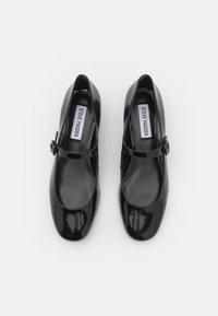 Chaussures Mary Jane en cuir verni noir avec un bout arrondi et une bride à boucle unique, étiquetées « Steve Madden », vues de dessus.