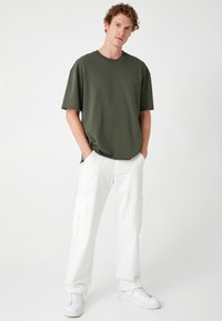 Oliven grøn oversized t-shirt med korte ærmer, parret med hvide cargo bukser med sidelommer og en afslappet pasform. Hvite sneakers.