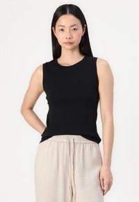 Black sleeveless top with a round neckline, made from smooth fabric, paired with light beige textured trousers featuring an elastic waistband.
