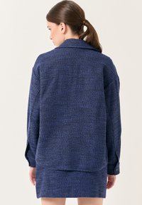 Giacca navale in tessuto testurizzato con design a collare, vestibilità ampia e dettagli con polsini bottonati, abbinata a una gonna coordinata.
