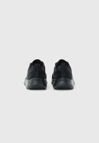 Une paire de chaussures de sport noires montrées de l'arrière sur un fond blanc, présentant des semelles épaisses et des languettes au niveau des talons.
