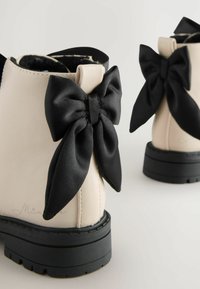 Beige Leder-Stiefeletten mit einer schwarzen Satinschleife an der Rückseite, strukturiertem Gummisohle mit leichtem Absatz und minimalistischem Design.