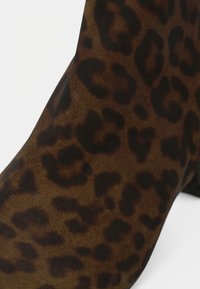 Botín de tobillo con estampado de leopardo en ante marrón y negro. Presenta una textura suave y una forma contorneada con un ligero tacón.