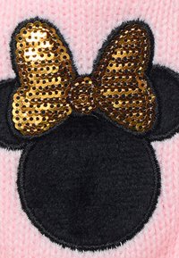 Applicazione in feltro nero a forma di testa con un fiocco in paillettes dorate su uno sfondo in maglia rosa. Le fibre testurizzate sono visibili nella zona rosa.
