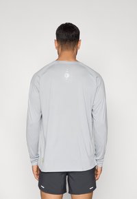 Αθλητική μπλούζα μακρυμάνικη σε ανοιχτό γκρι χρώμα με στρογγυλή λαιμόκοψη, διακριτική λεπτομέρεια λογότυπου στο πίσω μέρος και ραγκλάν μανίκια για άνεση στις κινήσεις.