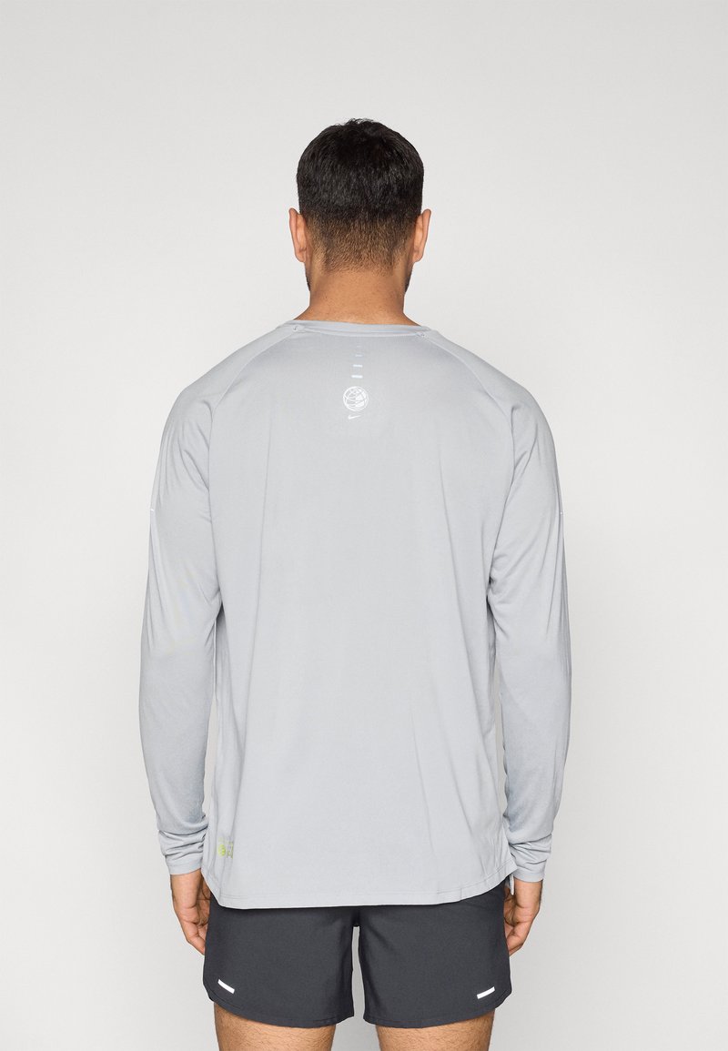 Maglietta sportiva a maniche lunghe color grigio chiaro con scollo rotondo, dettaglio sottile del logo sul retro e maniche raglan per facilitare i movimenti.