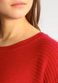 Rode gebreide trui met een gestructureerd patroon, voorzien van een brede halslijn en ribbelrandjes. Zacht materiaal met een comfortabele pasvorm.