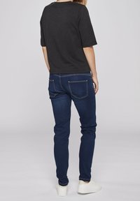 Schwarzes T-Shirt mit kurzen Ärmeln, kombiniert mit blauen Jeans, die fünf Taschen haben, und weißen Sneakern, von hinten betrachtet.