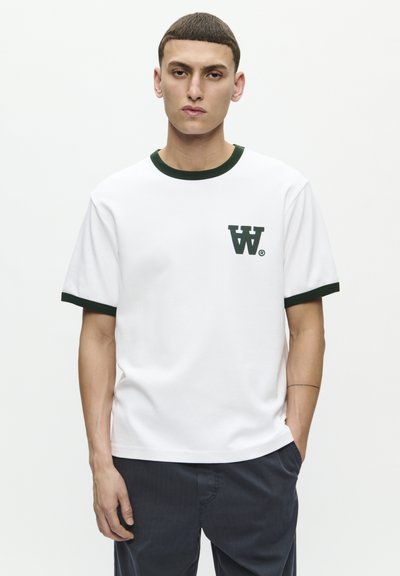 T-shirt bianca in cotone con rifiniture verdi attorno al collo e alle maniche, caratterizzata da un piccolo logo verde sul lato sinistro del petto. Maniche corte e vestibilità rilassata.