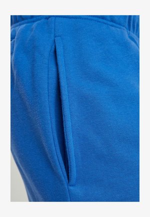 Puha szövetből készült kék jogger nadrág. Külső oldalzsebbel és rugalmas derékkal rendelkezik. Simára szőtt textúra, egyszínű.