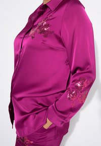 Satinbluse i livlig magenta med broderede blomster mønstre og perler på ærmerne. Har en klassisk krave og knaplukning.