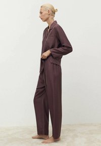 Completo pigiama in due pezzi di colore bordeaux realizzato in tessuto morbido. Presenta una camicia con colletto e tasca e pantaloni larghi con elastico in vita.
