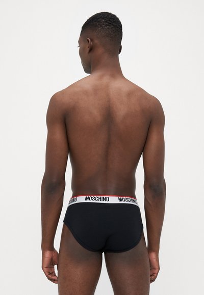 Schwarze Baumwollunterwäsche mit einem kontrastierenden weißen Bund und roter Schrift. Das Design umfasst eine enge Passform und minimale Nähte.