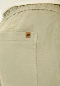 Beige bomuldsbukser med en syet lomme, der har et struktureret stof og et lille læderlogo-patch nær taljen.