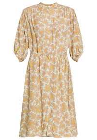 Květinové paisley šaty v krémové barvě s žlutými a růžovými vzory. Mají vysoký límec, nabírané rukávy a elastický pas pro zdůraznění postavy.