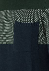 Pull en tricot avec des rayures horizontales vert foncé et gris clair, un motif texturé et une poche poitrine en vert foncé uni.