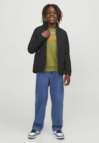Svart zip-up jacka, grön sweatshirt med orange text, blå denimjeans och svart-vita sneakers. Avslappnad passform med en avslappnad silhuett.