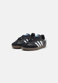 Zapatillas deportivas negras con parte superior de ante y cuero. Con rayas blancas, cordones negros y una suela de goma marrón texturizada.