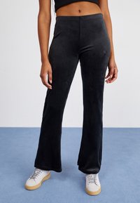 Black, flared sweatpants made of soft fabric with a smooth texture. Features a subtle logo detail near the waistband and ribbed hem.