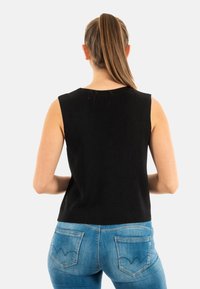 Top attillato senza maniche di colore nero con texture a coste e scollatura rotonda, abbinato a jeans in denim blu con cuciture distintive delle tasche.