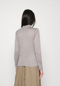 Jasnoszary, długi sweter z golfem, wykonany z miękkiego materiału dzianinowego, o dopasowanym kroju i lekko zaokrąglonym dolnym brzegu z tyłu.