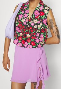 Zwart bloemen cropped vest met levendige roze en groene bloemen, gecombineerd met een lila mini rok met ruffles. Glad stofoppervlak overal.