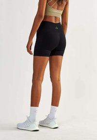 Black athletic shorts with a high waistband, textured fabric, and white logo detail. Paired with white athletic shoes and striped socks.