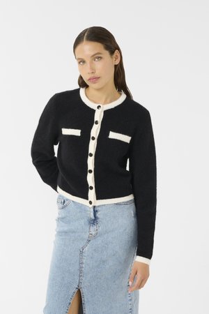 Black cardigan with white trim, featuring two front pockets and round neckline. Soft texture, button front closure, and standard fit.