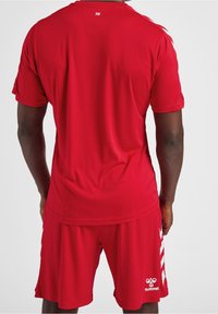 Červený sportovní dres s krátkým rukávem, vyrobený z lehkého materiálu. Na zadní straně se nachází logo a k dresu ladící červené šortky.