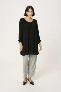 Schwarze, leichte Tunika mit gerafftem Ausschnitt und langen Ärmeln, kombiniert mit hellgrauen, schmal zulaufenden Hosen und schwarzen spitzen Ballerinas.