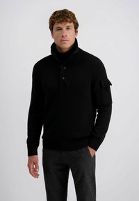 Zwarte gebreide trui met een hoge kraag, knoopsluiting aan de nek en geribbelde zoom. Bevat een patchzak op de linker mouw en een textuurstof.