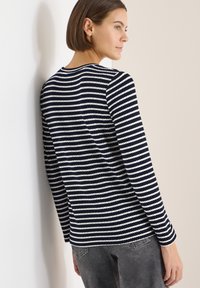 Top de punto de manga larga a rayas azul marino y blancas con cuello redondo y textura acanalada, combinado con vaqueros grises.