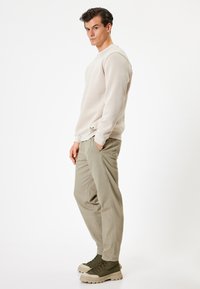 Lys beige sweatshirt med ribbede manchetter, parret med lyse grønne bukser og grønne støvler med en tyk sål. Glatte teksturer overalt.