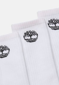 Weiße Socken mit gerippter Textur, die jeweils ein schwarzes Baumlogo aufweisen. Die Bündchen haben einen rosa Akzent. Drei Paar werden nebeneinander angezeigt.