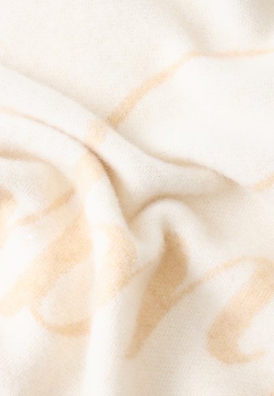 Tela blanca suave con patrones abstractos ondulados en beige claro y pliegues suaves que muestran textura y material acogedor.