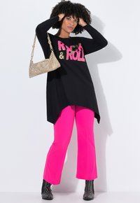 Tunique noire à manches longues avec impression "Rock & Roll", pantalon évasé rose vif, et un sac à main doré brillant qui accentue l'ensemble.